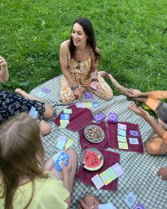 Group of adults sitting on picnic blankets in the grass, playing The Well-being Game with cards spread out between them.