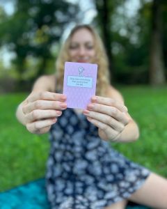 Woman outdoors holding up a card from The Well-being Game toward the camera.
