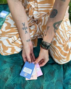 Woman sitting cross-legged on a blanket arranging several The Well-being Game cards on the ground.