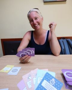 Woman sitting at a wooden table playing The Well-being Game, with cards spread out in front of her.