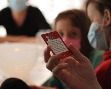 Child and adult wearing masks looking at a red card from The Well-being Game during indoor play.