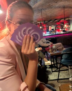 Woman in a bar holding several The Well-being Game cards in front of her face while sitting at a table.