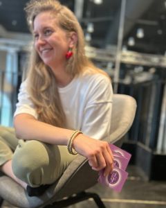 Woman seated indoors holding cards from The Well-being Game while smiling during gameplay.